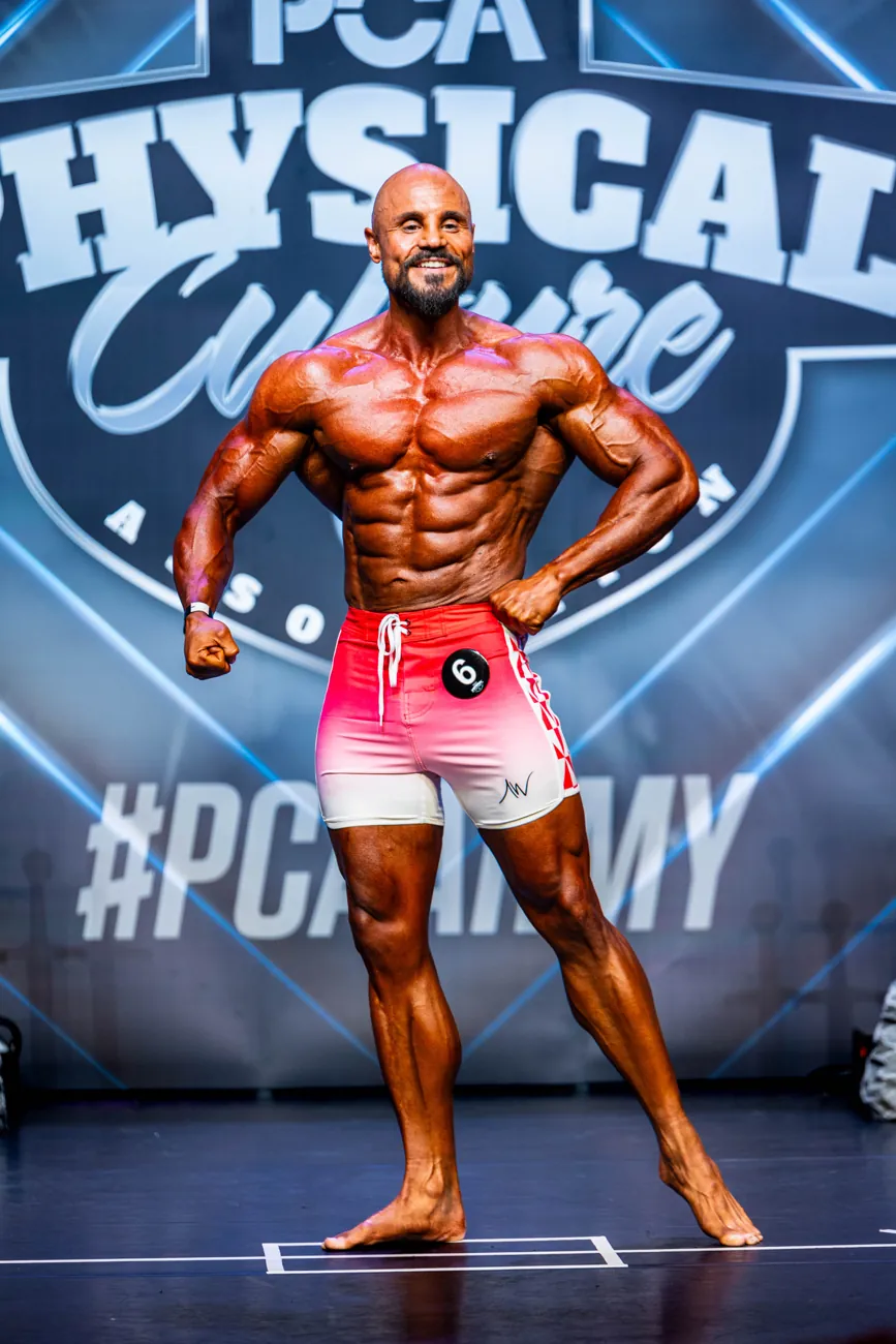 Men's physique athlete posing on stage in red shorts